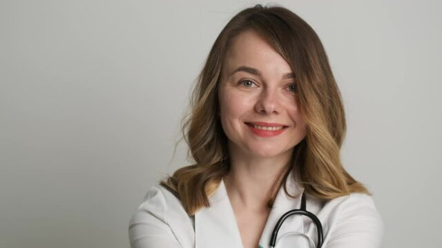 Woman doctor nutritionist in medical gown sitting at the table smiling at camera holding carrots and measuring tape