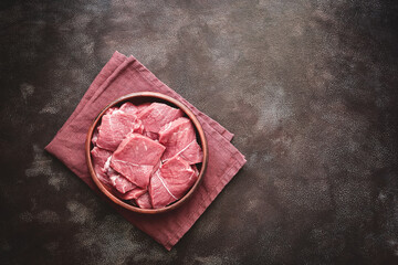 Fototapeta na wymiar Pieces of fresh raw beef meat in a bowl on brown dark background. Top view, flat lay, copy space.