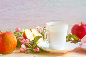 On a wooden background, a branch of apple flowers, a mug with tea, marshmallows and red apples. Still life. Close-up, food and spring concept, postcard. Copy space, space for text.