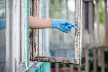 A woman hand in medical protective glove opens a house window close up.