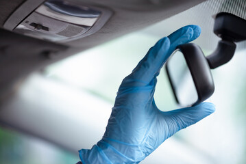 Woman in medical gloves is looking into a car mirror close up.