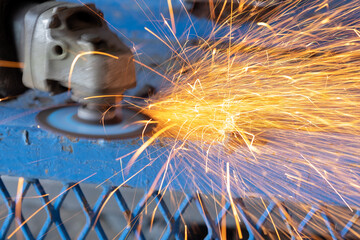 worker cutting steel with grinding machine and splashes of sparks in workshop.