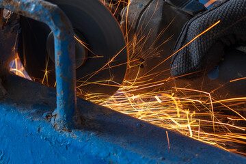 worker cutting steel with grinding machine and splashes of sparks in workshop.