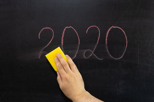 Hand wipes the inscription 2020 from the chalkboard
