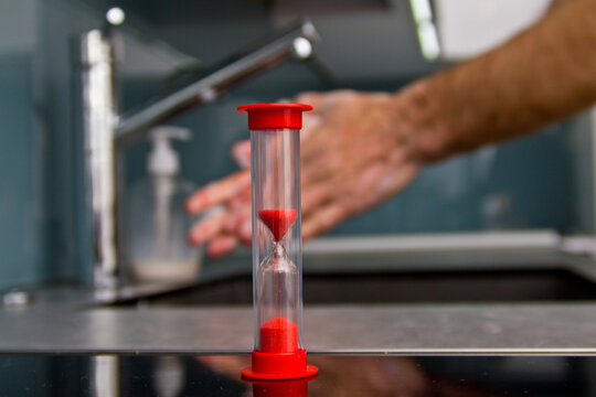 Man washes his hands with soap and uses an hourglass to measure hand washing time