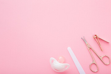 Scissors, clipper, nails file and soother on light pink table background. Pastel color. Baby nails grooming. Closeup. Empty place for text. Top down view.