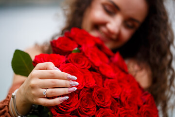 Fototapeta na wymiar Hand of a girl with a wedding ring close-up on a bouquet of red roses