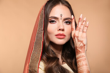 Mehendi. Portrait of beautiful indian girl in saree isolated on beige. Young hindu woman model with kundan golden jewelry set. Traditional Indian costume lehenga choli. Henna painting on hand.