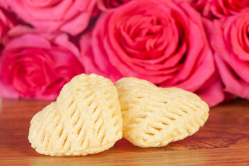 Two hearts in the shape of a potato chip on a wooden background with pink roses