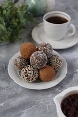 cake balls with coconut flakes and cocoa on white retro plate on light background with a cup of coffee, flowers and strawberry jam