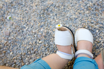 Fototapeta premium Tiny white summer shoes on a baby child with a yellow flower on a stone background