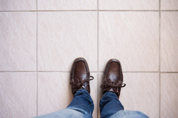 Legs in Jeans and brown leather shoes against tiled floor. Concept of waiting with space for text.