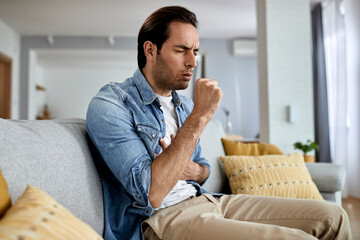 Young man coughing while sitting in the living room.