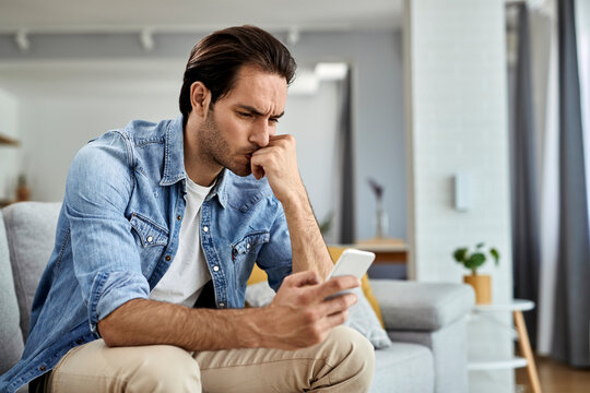 Distraught Man Reading Text Message On Cell Phone At Home.