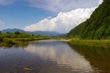 Naklejka na ściany i meble landscape with mountain river and cumulus clouds on a summer day before rain