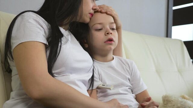 Mother hugs her sick son. The child measures the temperature. Mother stroking her son on the head.
