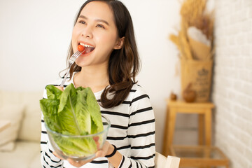 Young asian woman and happy   eating healthy salad sitting on the table with green fresh ingredients indoors.greens in bowl for breakfast or lunch. Vegan vegetarian healthy food.