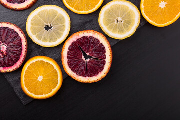 Fototapeta na wymiar Fresh ripe citruses. Lemons, red oranges and oranges on dark stone background. Copy space