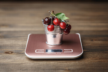 Sweet cherry in small decorative metal bucket standing on a cooking scale © Volodymyr Herasymov