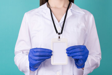 Close-up cropped photo of female doctor in gloves wearing white coat biohazard hazard uniform a blank empty mock up nametag isolated on blue teal background