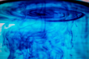 Fototapeta na wymiar Blue ink spilled in water. A swirl of paint on the surface of the liquid