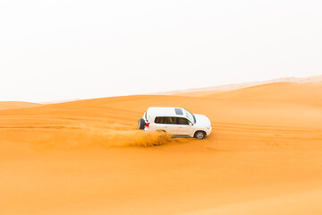 Off-road white SUV vehicle car speeding through the desert sand dunes in the UAE. Safari tour.