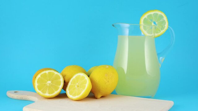 Fresh squeezed lemonade and sliced lemons on cutting board on blue background 