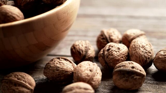 Fresh walnut kernels and whole walnuts in a bowl on rustic old wooden table in 4K VIDEO. Healthy organic food, BIO viands, natural background concept.