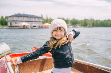 A little girl with blond hair of European appearance posing on a boat on the river.