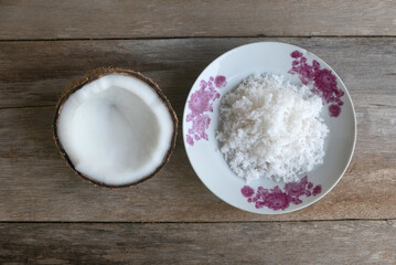 Top view of coconut and coconut flakes in a plate on a wooden background.