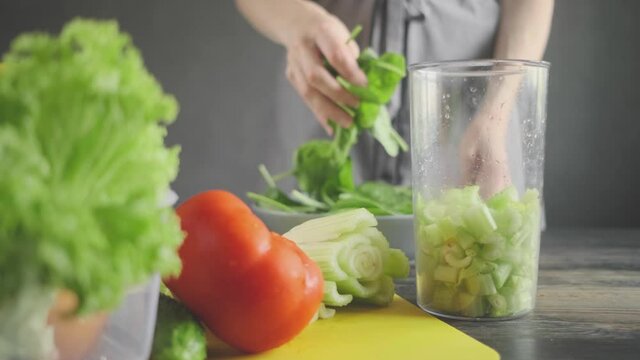a woman prepares slices on a cutting board ingredients for a celery and spinach smoothie and puts them in a blender bowl