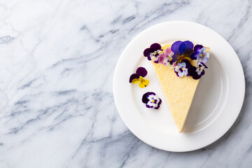 Cheesecake decorated with edible flowers on white plate. Marble background. Copy space. Top view.