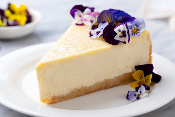 Cheesecake decorated with edible flowers on white plate. Marble background. Close up.