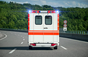 Rear view of a single ambulance car on a highway with blue emergency lights