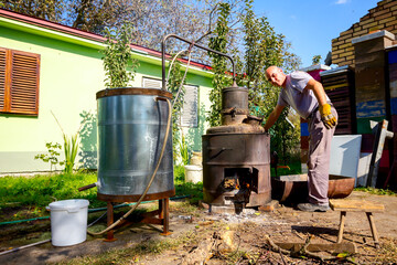 Man is manually mixing fruit marc in distillation apparatus for making domestic alcohol liquor