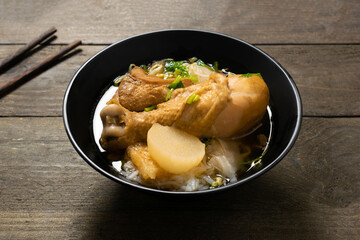 Rice noodle with chicken leg in black bowl on wooden table.