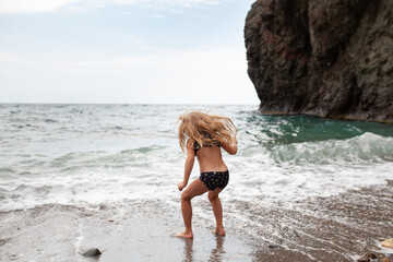 Happy pretty girl walks along the sea coast against the background of the sea, from behind a beautiful landscape