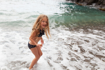 Obraz premium Happy pretty girl walks along the sea coast against the background of the sea, from behind a beautiful landscape