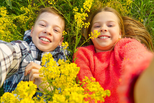 Happy smiling kids making self portrait on smartphone in meadow. young boy and girl making selfie on smartphone laying in green grass with yellow flowers.