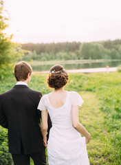 outdoor portrait of young happy beautiful newlyweds walking at green lawn
