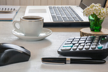 Cup of coffee, laptop with mouse, notebook with pen and calculator on white desktop