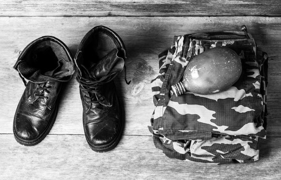 old leather black men's army boots, military uniform and water flask on a wooden background close-up view from above, black and white photo