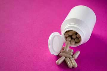 Spilled medical pills from white pill bottle on pink background