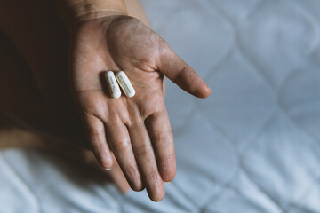 Two white capsules in a woman's hand while sitting on the bed. Happy pill capsule, Anti sorrowful capsule.