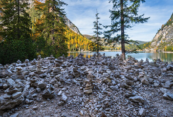 Small stone pyramides near autumn peaceful alpine lake Braies or Pragser Wildsee, South Tyrol, Dolomites Alps, Italy. Picturesque traveling, seasonal and nature beauty concept scene.