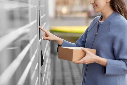 mail delivery and post service concept - close up of happy smiling woman with box at outdoor automated parcel machine choosing operation on touch screen