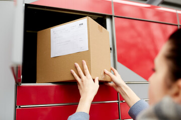 mail delivery and post service concept - woman putting box to automated parcel machine