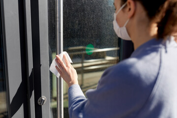 Obraz premium hygiene, health care and safety concept - close up of woman in mask cleaning outdoor door handle with antiseptic wet wipe