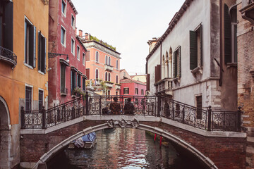 Fototapeta na wymiar Two lovers sitting side by side on a bridge over a canal among pink buildings in Venice, Italy