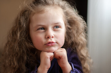 Closeup portrait of a cute toddler girl with her curly hair at home near the window